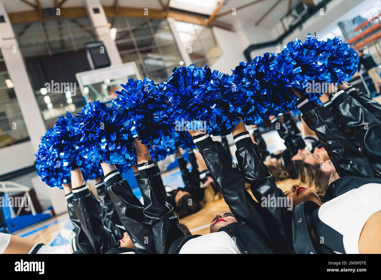 Vista laterale delle cheerleaders che si posano sul campo da basket e che tengono i loro pom blu in cerchio. Foto di alta qualità Foto Stock