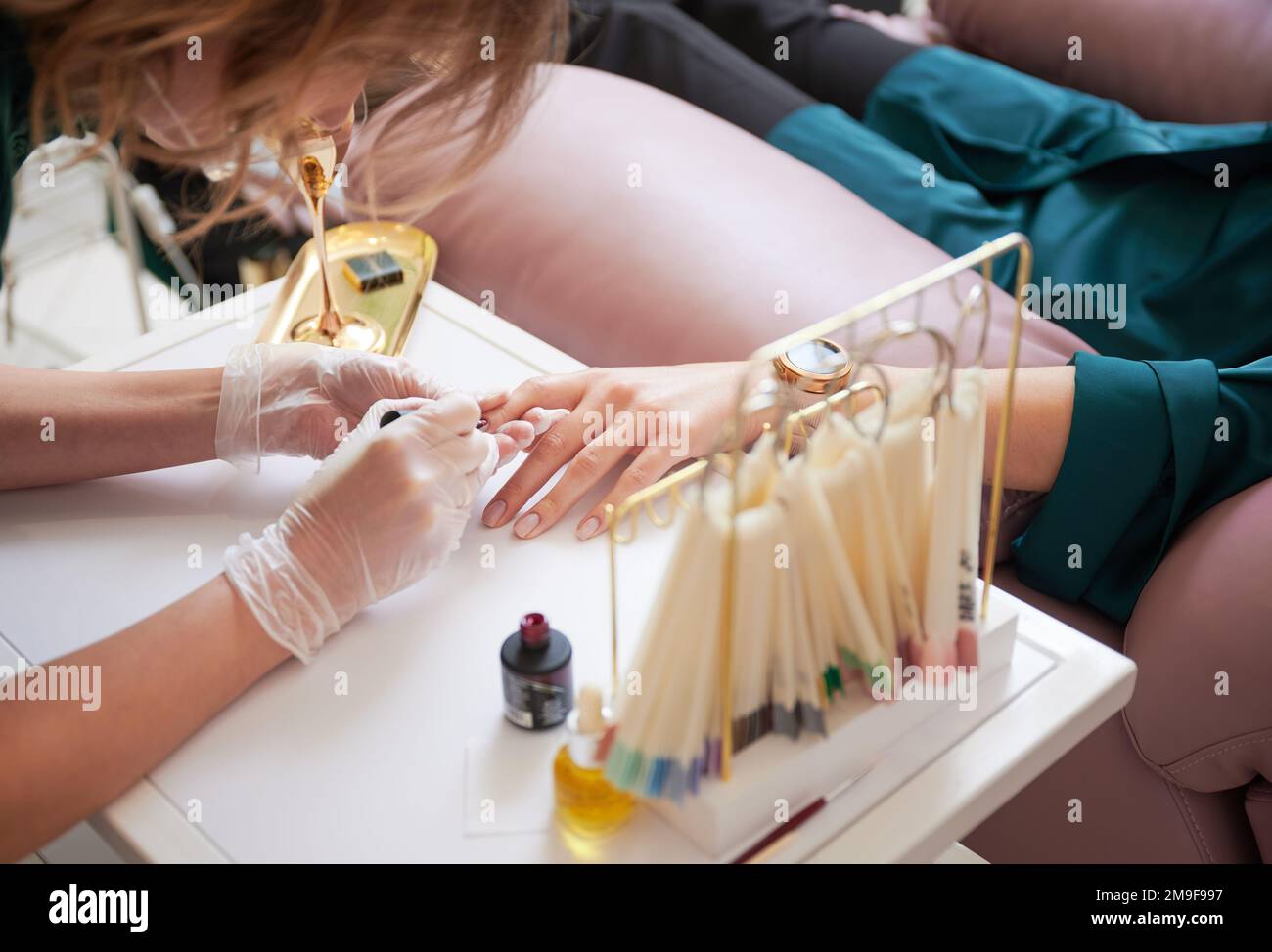 Manicure professionale per donna cliente in salone di bellezza. Primo piano di uno specialista di manicure in guanti sterili applicando smalto unghie rosso sulle unghie delle donne. Foto Stock