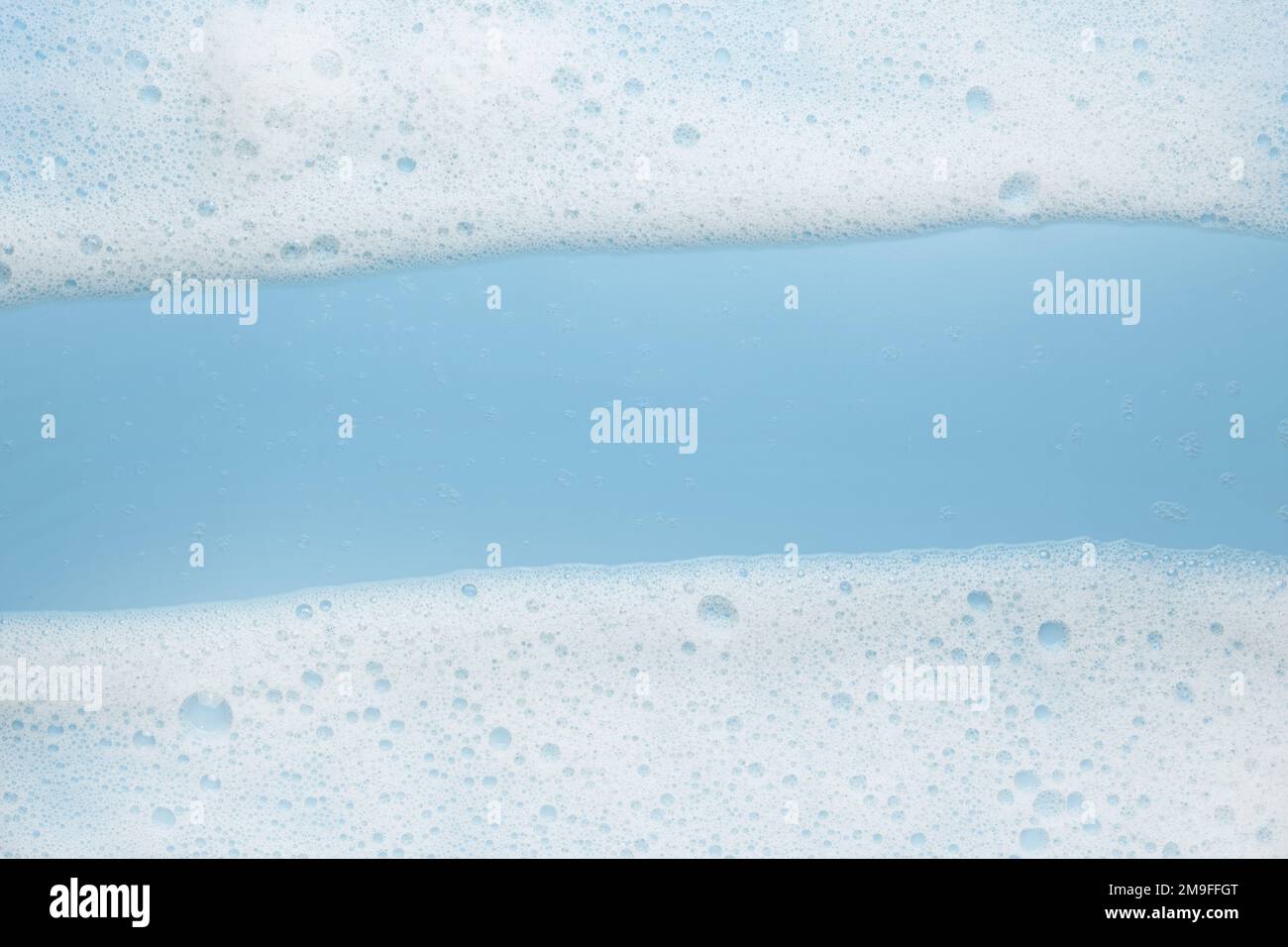 Mousse di schiuma bianca su sfondo blu. Cornice o bordo per il testo espanso. Il concetto di prodotti schiumogeni, cosmetici o detergenti. Foto Stock