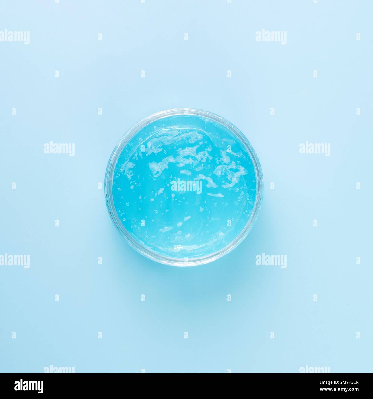 Gel liquido trasparente per la pulizia del viso in un vaso trasparente su sfondo blu. Prodotto cosmetico idratante per la cura della pelle o dei capelli. Foto Stock