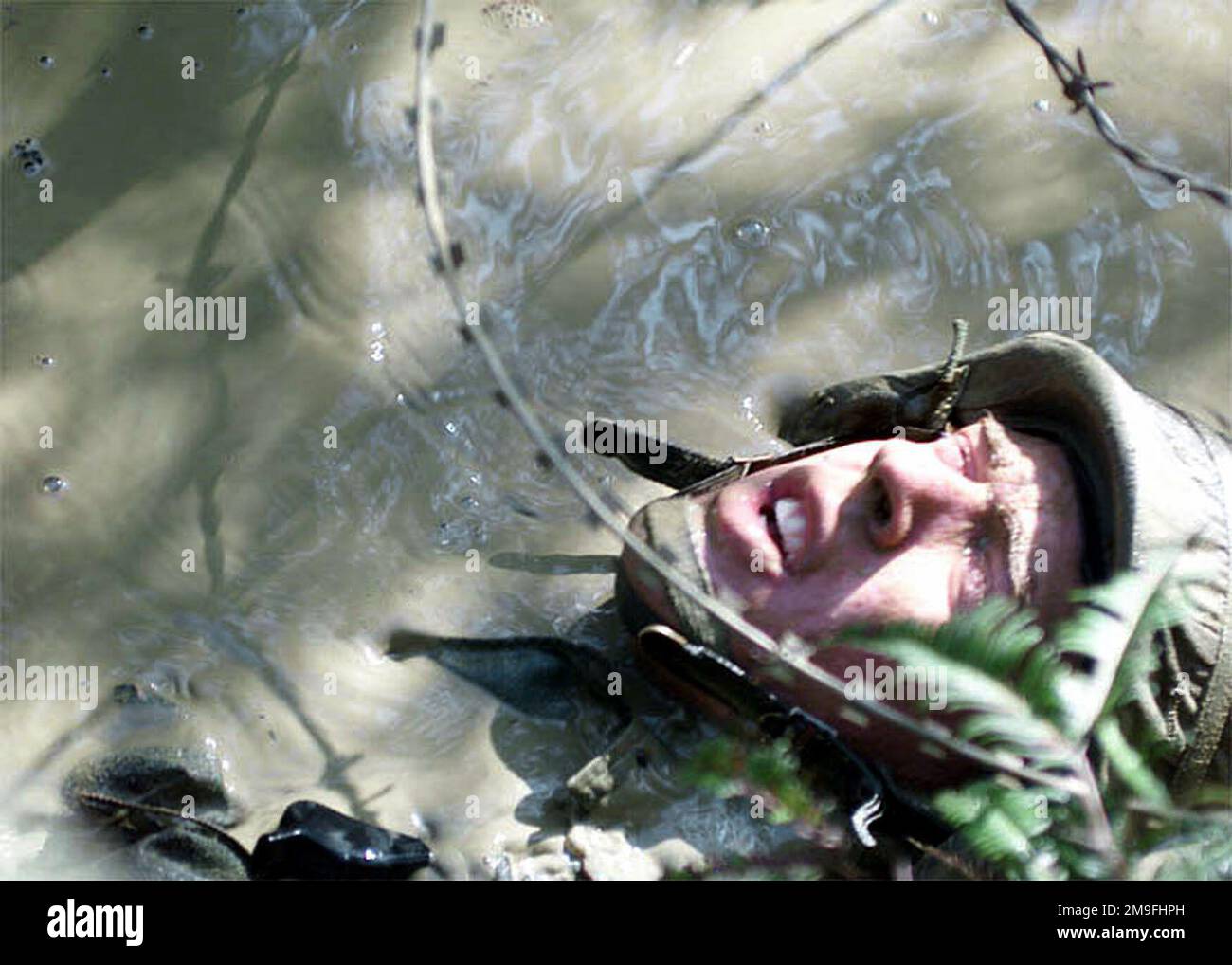 US Marine Corps Corporal (CPL), Andy Fouch con 3D Marine Division Communication Company, striscia indietro attraverso il fango mentre cerca di evitare il filo di concertina, durante il corso di resistenza a Camp Courtney, Okinawa, Giappone. Il JWTC è un'area di allenamento in cui Marines si esibisce in abilità di navigazione terrestre, tattiche di pattugliamento, ricognizione con la forza e abilità di sopravvivenza nella giungla. Subject Operation/Series: FOAL EAGLE 2000 base: Camp Courtney Stato: Okinawa Paese: Giappone (JPN) Foto Stock