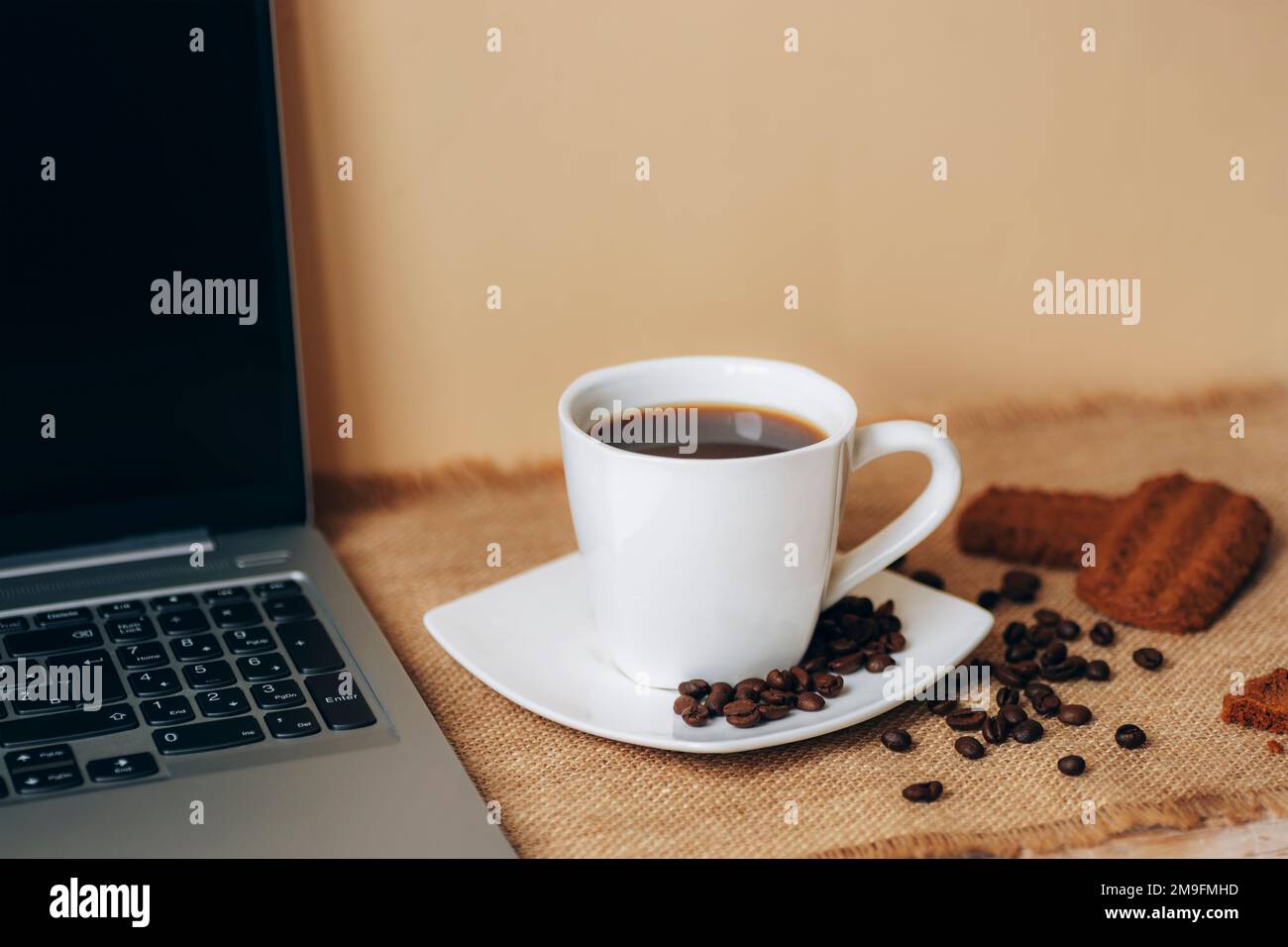 Tazza di caffè con fagioli, biscotti e computer portatile su un tavolo beige. Foto Stock