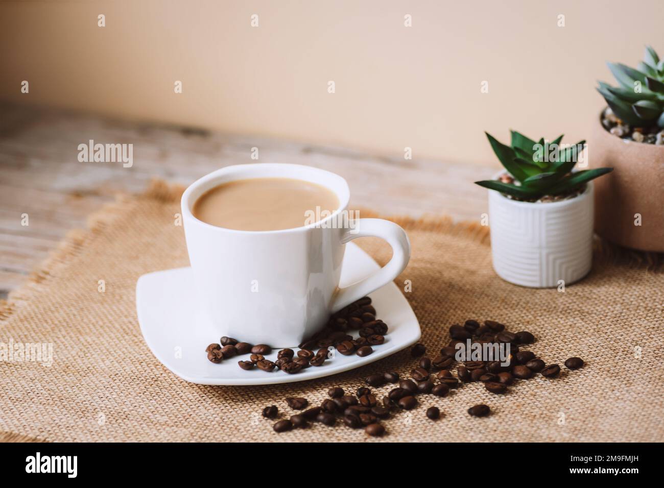 Latte di caffè in tazza bianca, chicchi di caffè su tovagliolo di tela da sacco. Primo piano. Foto Stock