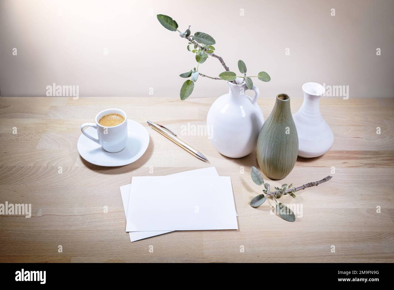 Tre vasi, ramo di foglia di salvia e tazza di caffè, mock-up di biglietti d'auguri bianchi su un tavolo di legno o scrivania contro una parete beige chiaro, tranquillo home Office Foto Stock