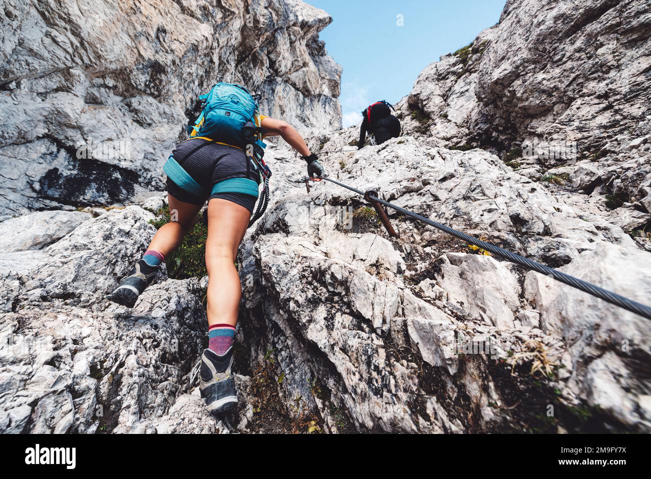 Vista dalla schiena guardando in alto la donna alpinista in pantaloncini che salgono sul sentiero via ferrata nelle Alpi Foto Stock