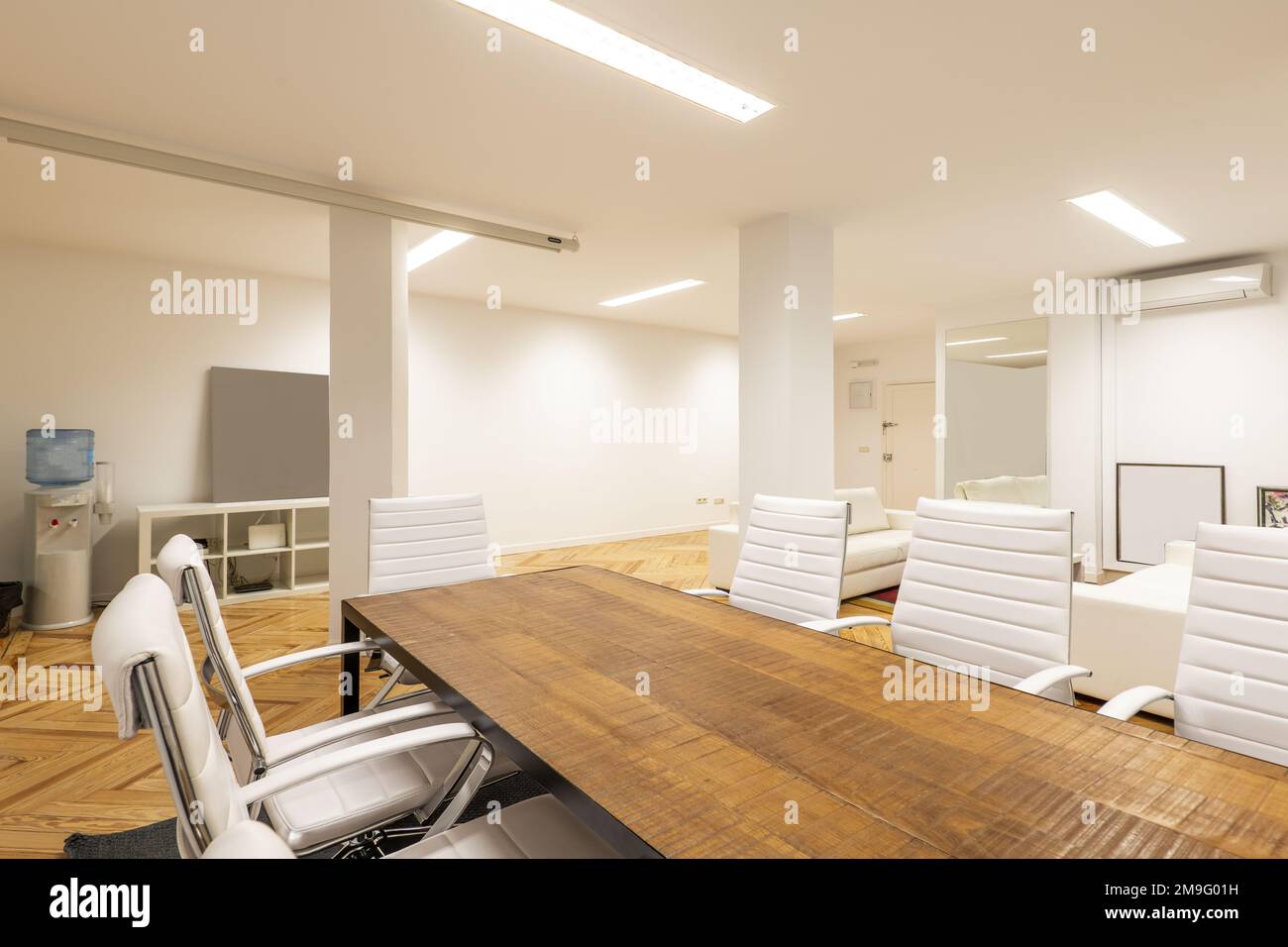 Un ufficio con un tavolo da riunione in legno di stile industriale con sedie girevoli rivestite in similpelle bianca Foto Stock