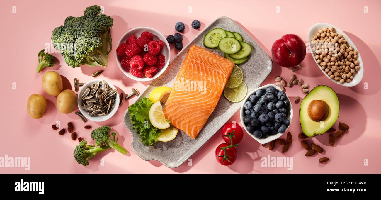 Vista dall'alto del delizioso salmone con cetrioli a fette e limoni serviti sul piatto vicino a frutta e frutti di bosco assortiti su sfondo rosa Foto Stock