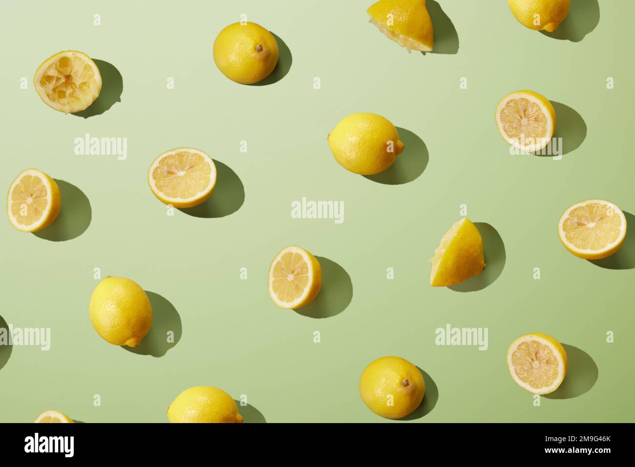 Dall'alto di limoni freschi maturi tagliati a metà e interi gialli disposti su una superficie verde come sfondo astratto Foto Stock