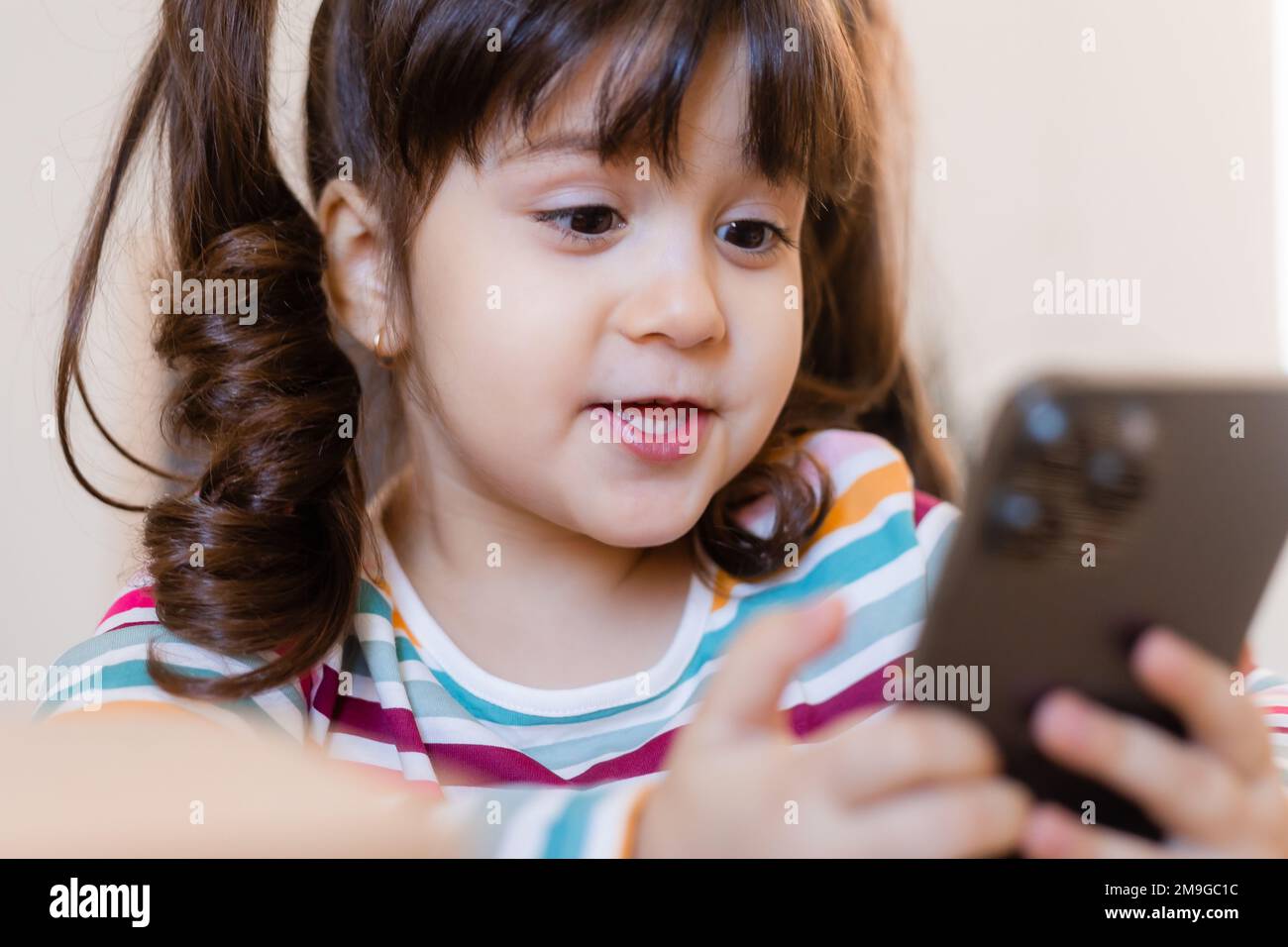 una ragazza piccola cute è agganciata con un insegnante in linea dal telefono. Educazione online dei bambini. Preschoolers e gadget Foto Stock