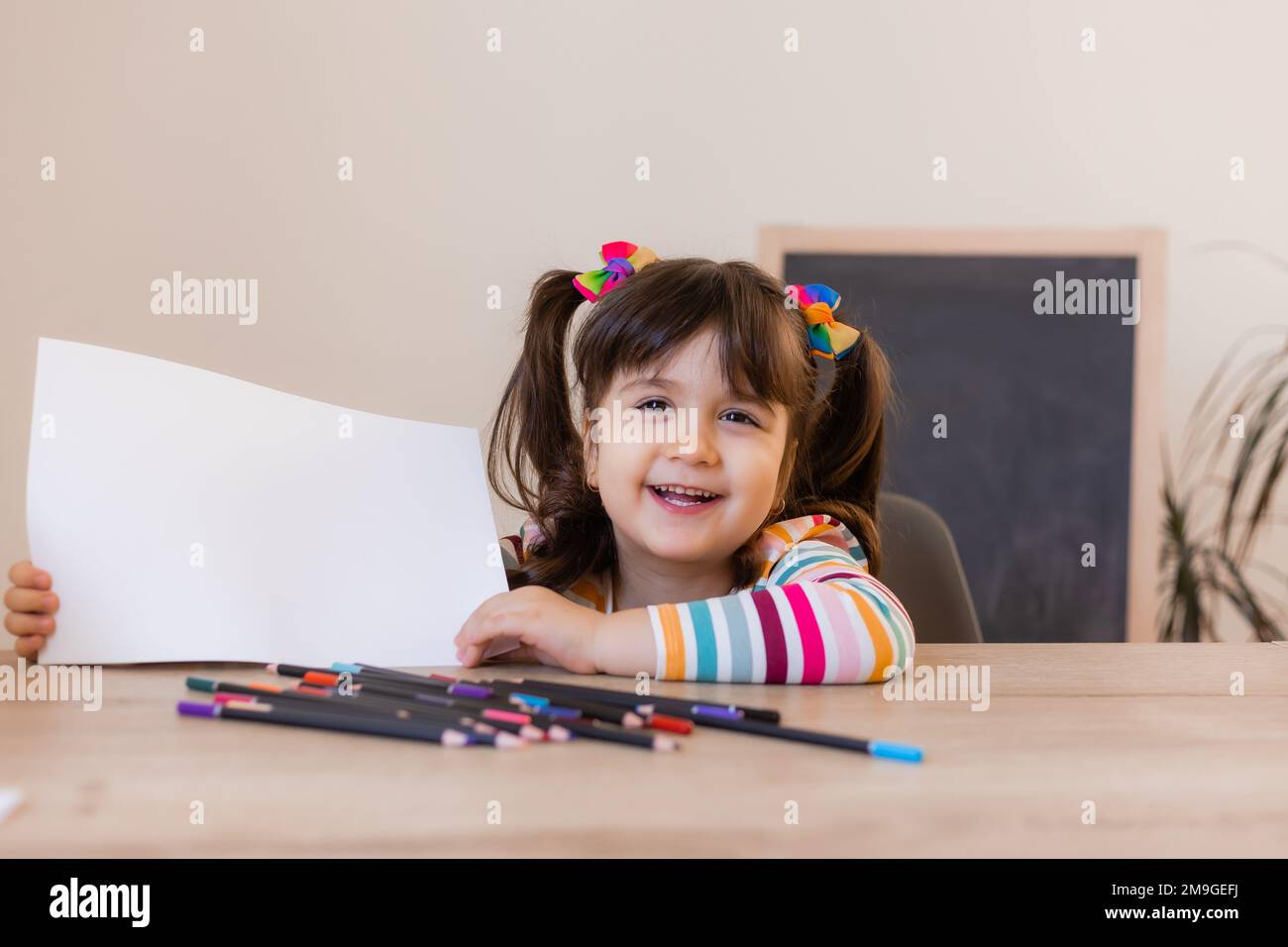 una bambina carina in una lezione di disegno tiene un foglio bianco vuoto nelle sue mani, uno spazio per il testo. Bambini e creatività Foto Stock