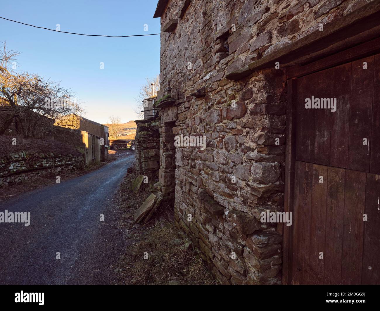 Primo piano dei tradizionali edifici in pietra con cielo blu luminoso, colline lontane e ruvida pista agricola in primo piano. Marsett, North Yorkshire Foto Stock
