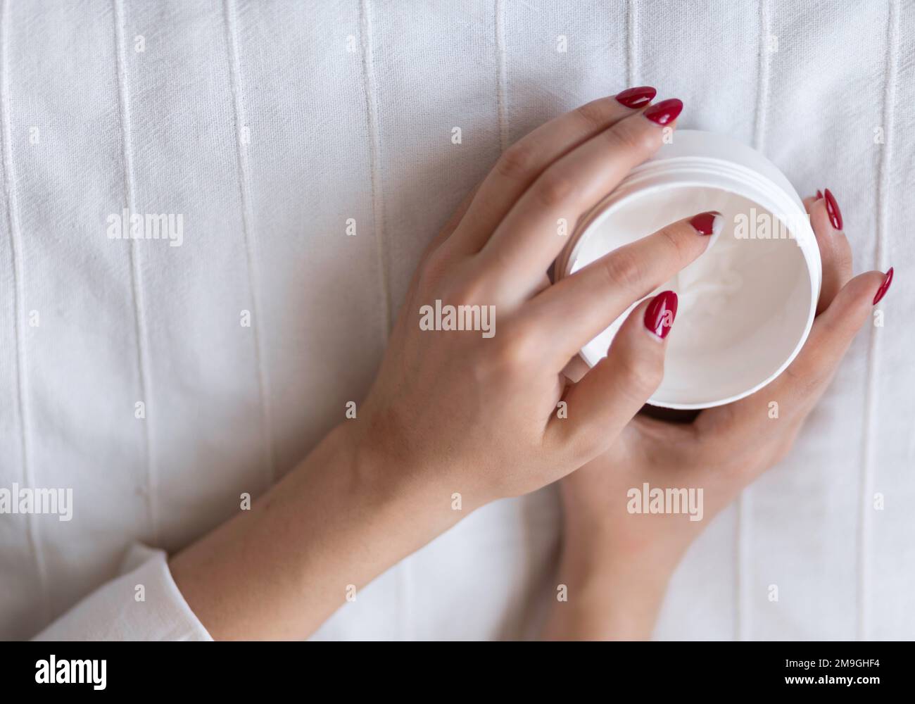 Belle mani di donna con vaso crema sulla coperta. Crema idratante per una pelle pulita e morbida. Ama un corpo. Concetto di assistenza sanitaria. Foto Stock