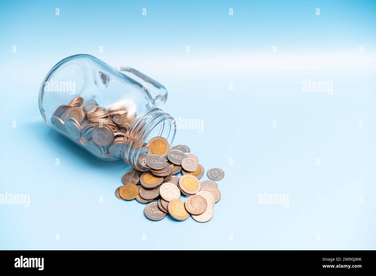 Un sacco di moneta flusso di denaro dal vaso di vetro su sfondo blu, risparmio di denaro concetto. Foto Stock