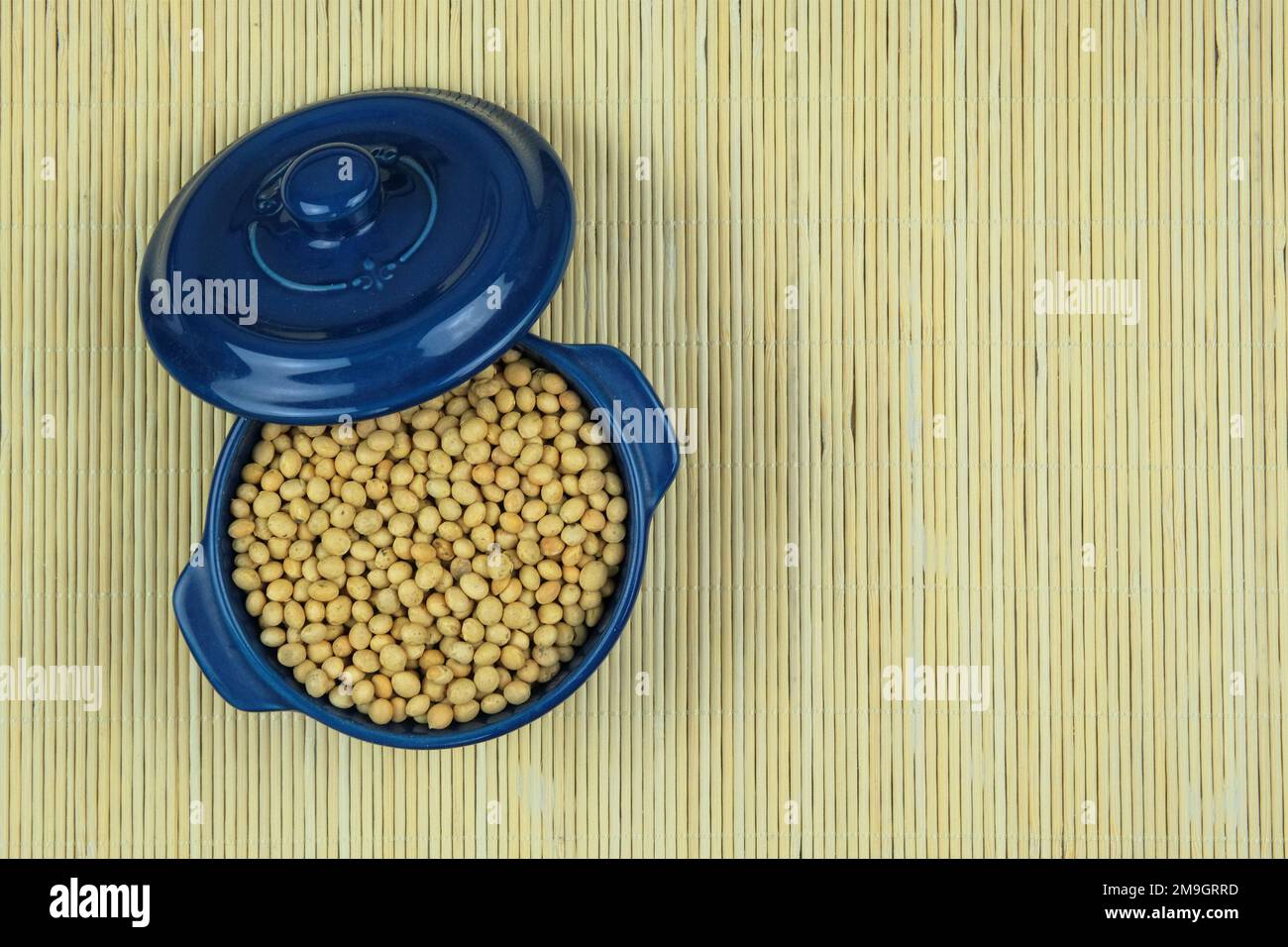 Soia in ciotola blu su fondo paglierino. Impulso proteico che viene essiccato e poi imbevuto e cotto prima di mangiare. Prodotto vegetariano. Vista dall'alto. Foto Stock