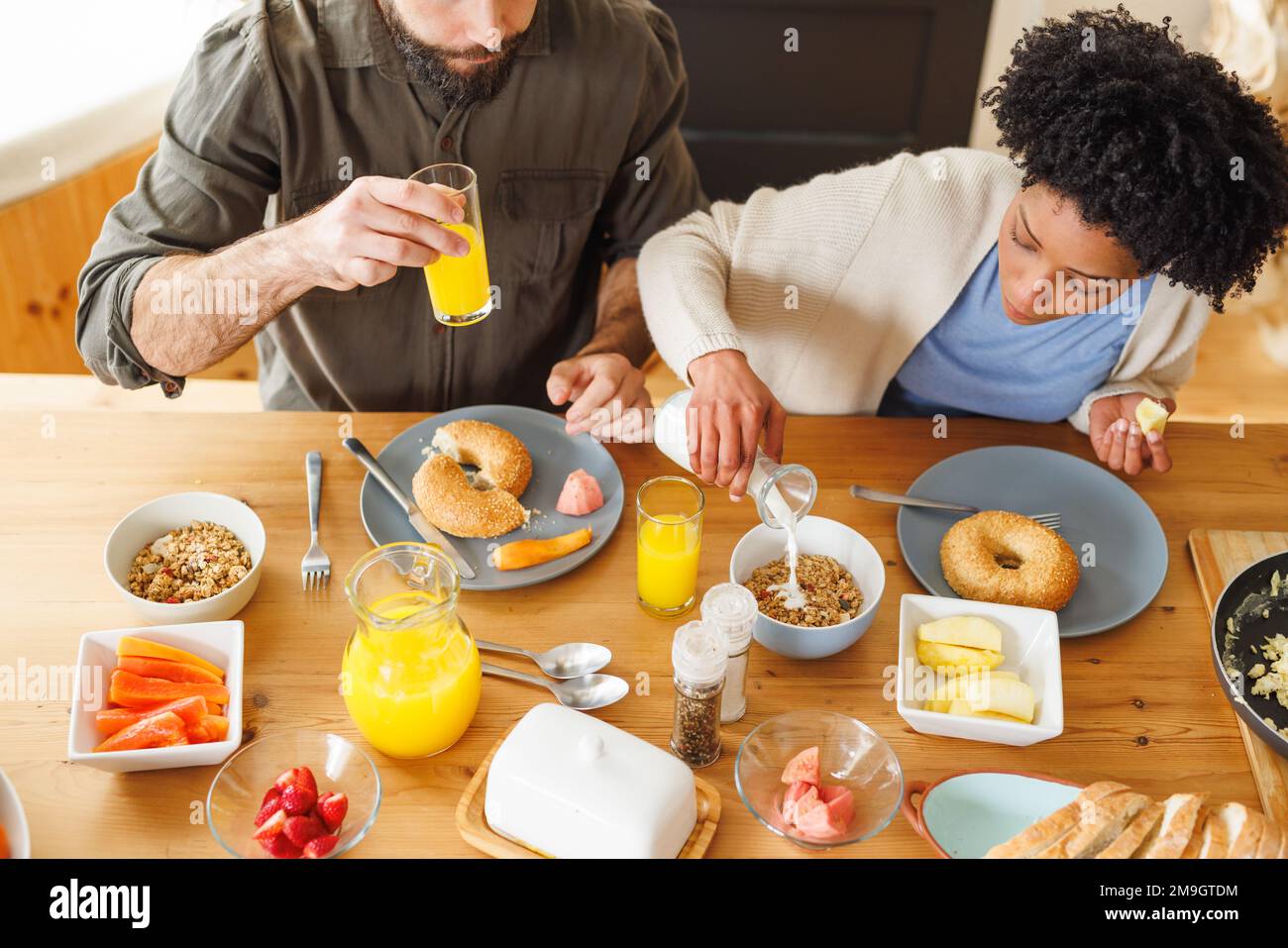 Vista dall'alto della giovane coppia biraciale che serve la colazione insieme sul tavolo da pranzo a casa Foto Stock