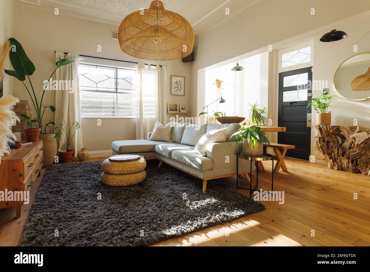Lampada a sospensione in rattan sospesa su divano, sgabello ottomano, piante da casa e moquette nel soggiorno Foto Stock