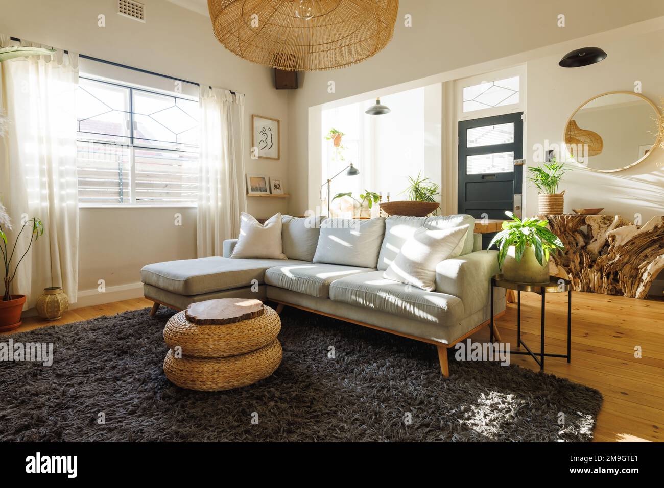 Lampada a sospensione in rattan sospesa su divano, sgabello ottomano, piante da casa e moquette nel soggiorno pulito Foto Stock