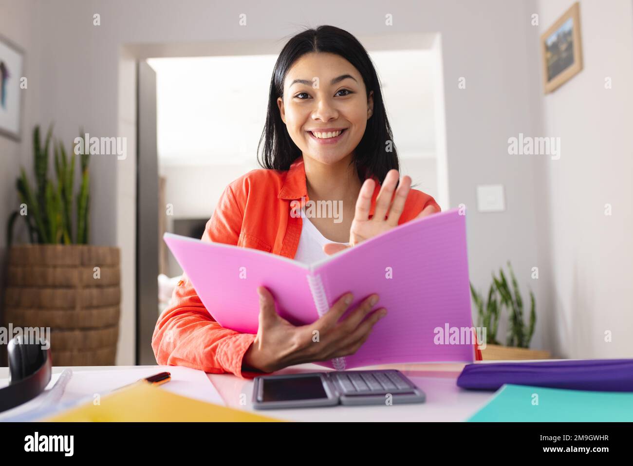 Immagine di una donna biraciale sorridente che tiene una lima rosa seduta al tavolo Foto Stock