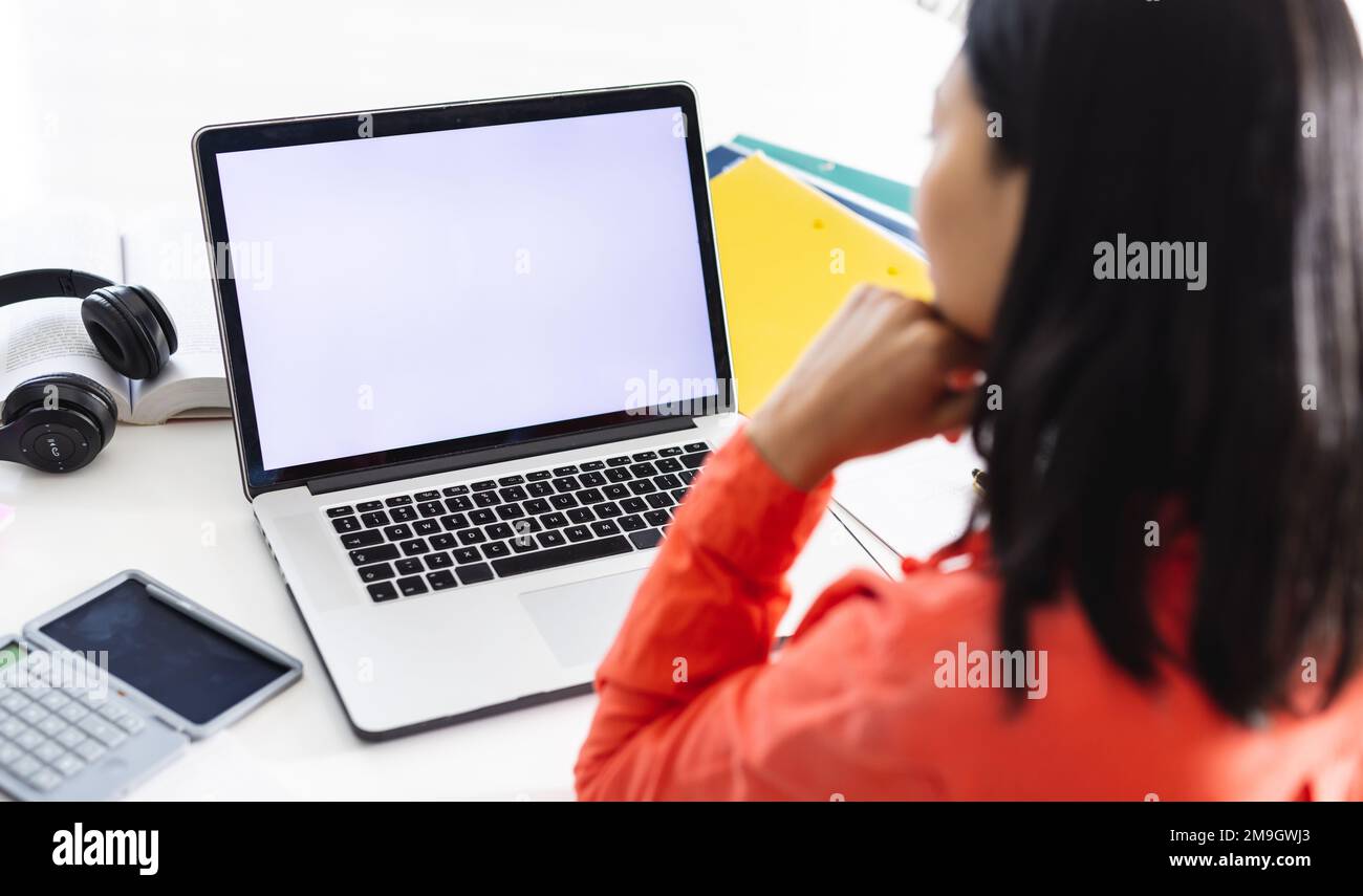 Immagine di una donna biraciale che utilizza un computer portatile con spazio copia sullo schermo seduto alla scrivania Foto Stock