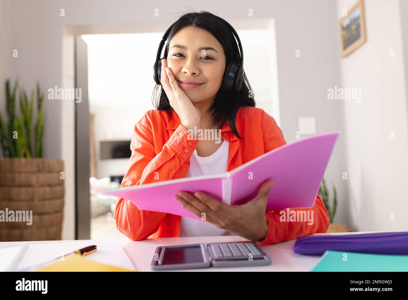 Immagine di una donna biraciale che utilizza cuffie che tengono una lima rosa seduto alla scrivania Foto Stock