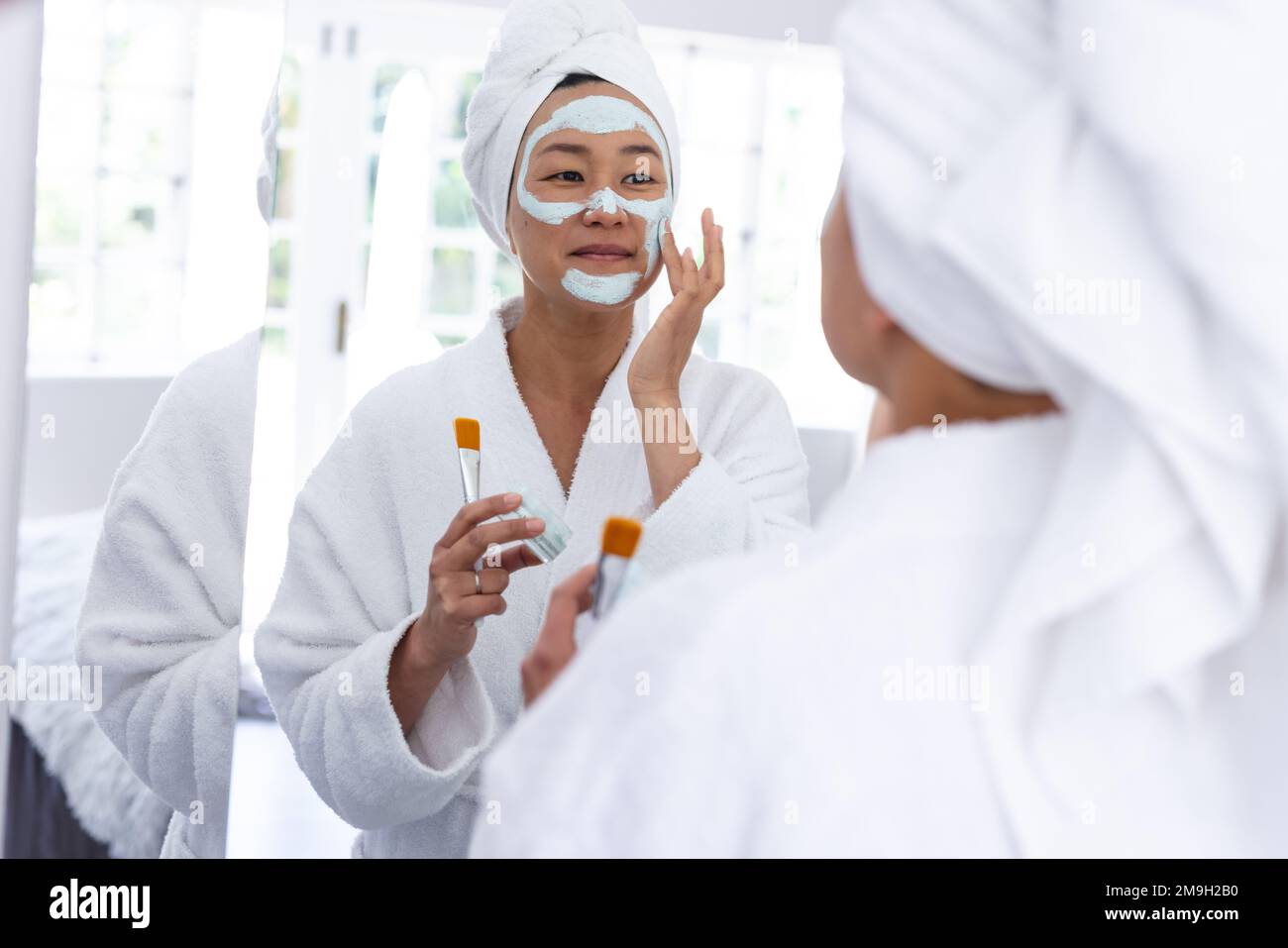 Donna asiatica felice applicando la maschera di bellezza del viso in bagno Foto Stock