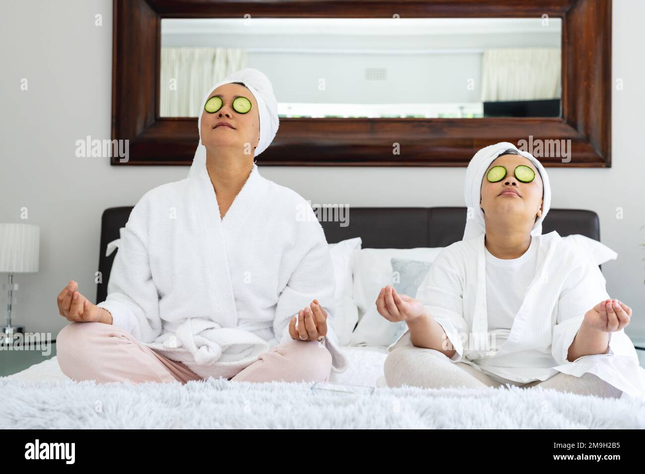 Buona madre asiatica e figlia seduta a letto e meditare Foto Stock