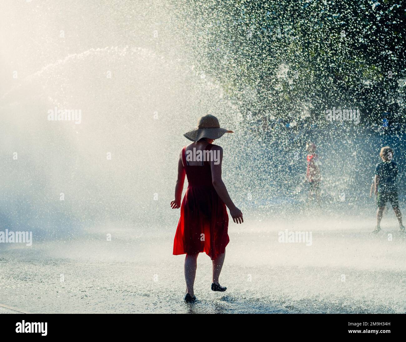 Donna in vestito rosso in piedi sotto acqua caduta in fontana, International Fountain, Seattle, Washington state, USA Foto Stock