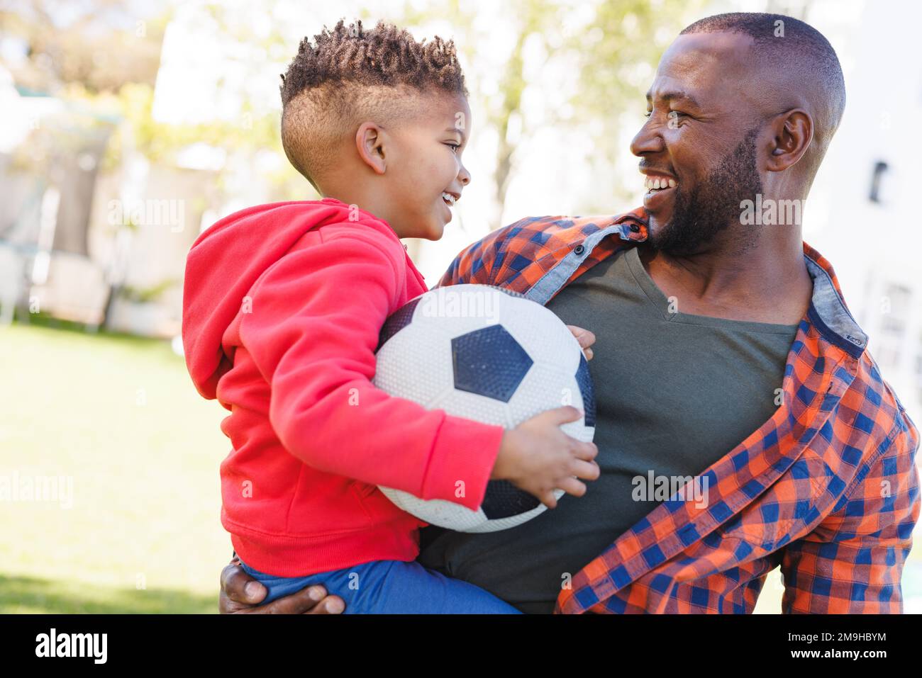 Buon padre e figlio afroamericano che gioca a calcio nel loro cortile Foto Stock