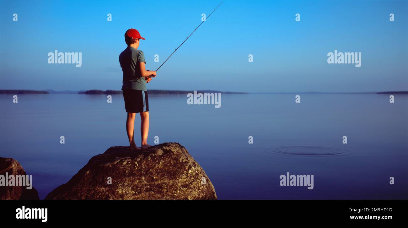Ragazzo che pesca da massi sulle rive del lago Pielinen, Lieksa, Carelia settentrionale, Finlandia Foto Stock