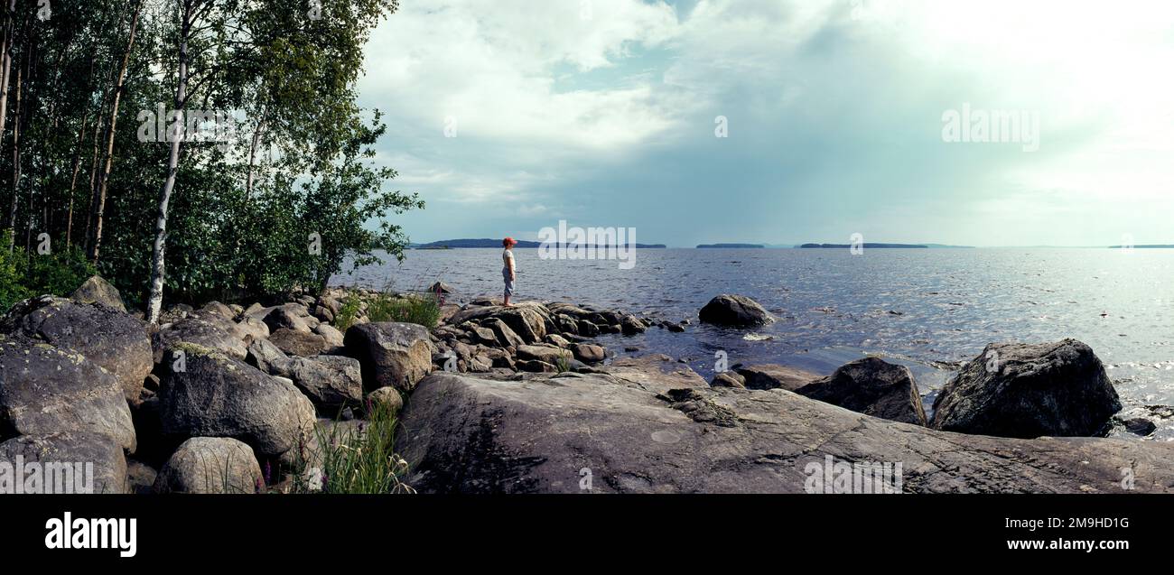 Paesaggio con ragazzo in piedi sulla riva rocciosa del Lago di Pielinen, Lieksa, Carelia Nord, Finlandia Foto Stock