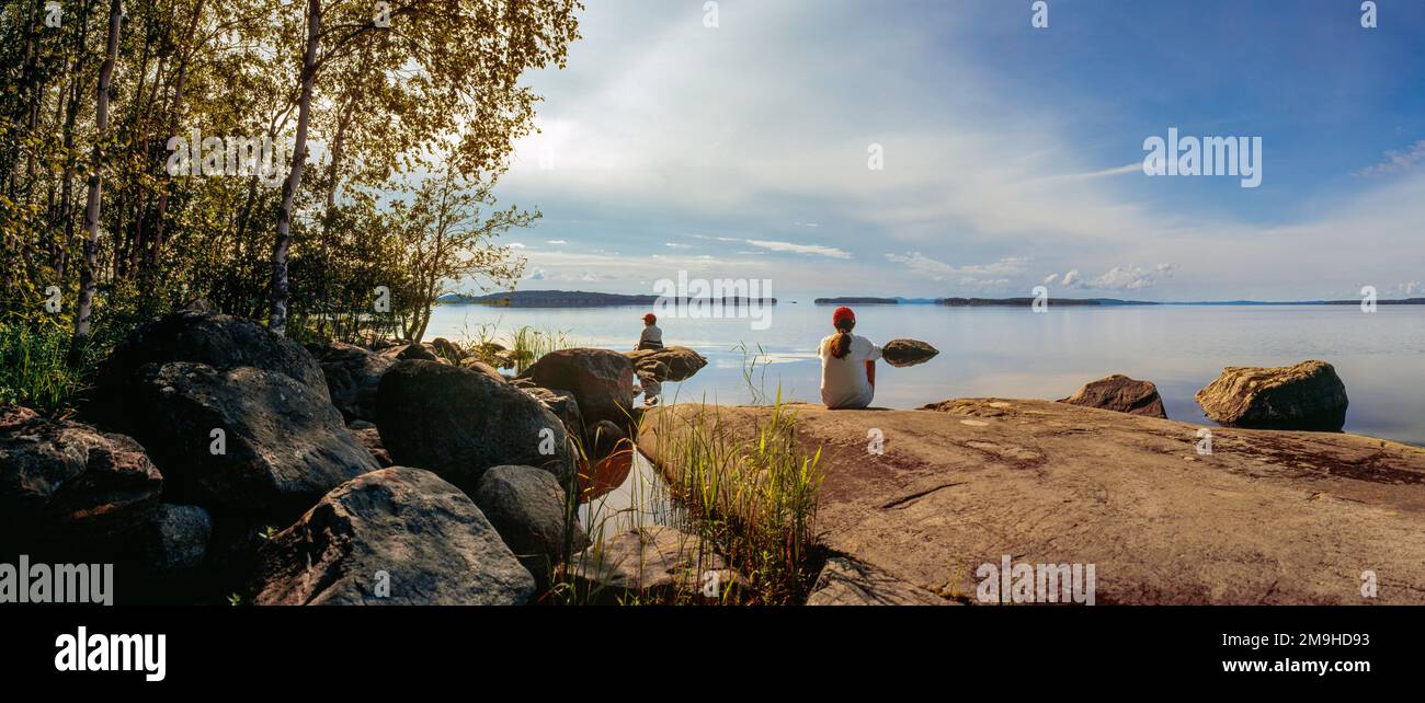 Ragazzo e ragazza seduti sulla riva rocciosa del lago Pielinen, Lieksa, Carelia settentrionale, Finlandia Foto Stock