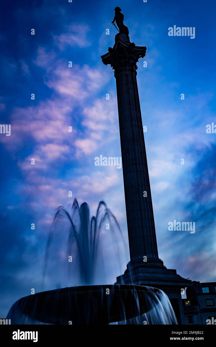 Trafalgar Square con la colonna di Nelson e la scenografica fontana contro un cielo blu scuro e suggestivo. Nuvole bianche e rosa e retroilluminazione aggiungono un tocco di drammaticità Foto Stock