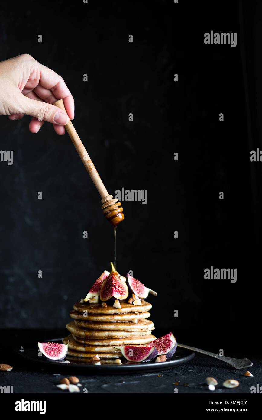 Pila di pancake con fichi, noci e miele scorrevole. Fatto in casa. Sfondo scuro. Frittelle di latticini soffici con fichi e sciroppo versando sopra. Delizioso Foto Stock