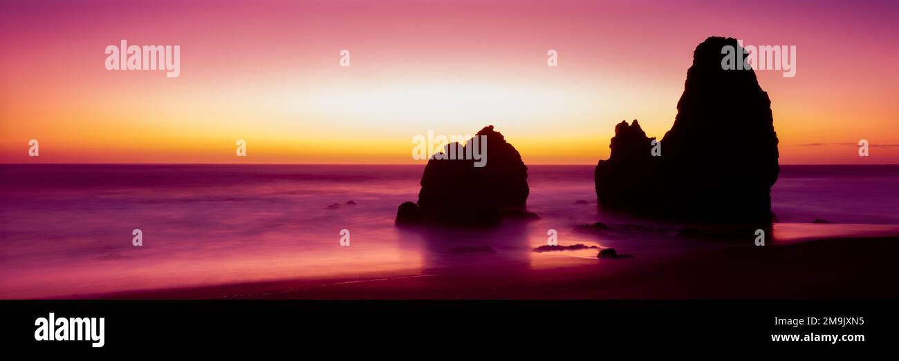 Sagome di formazioni rocciose sulla spiaggia al tramonto Foto Stock