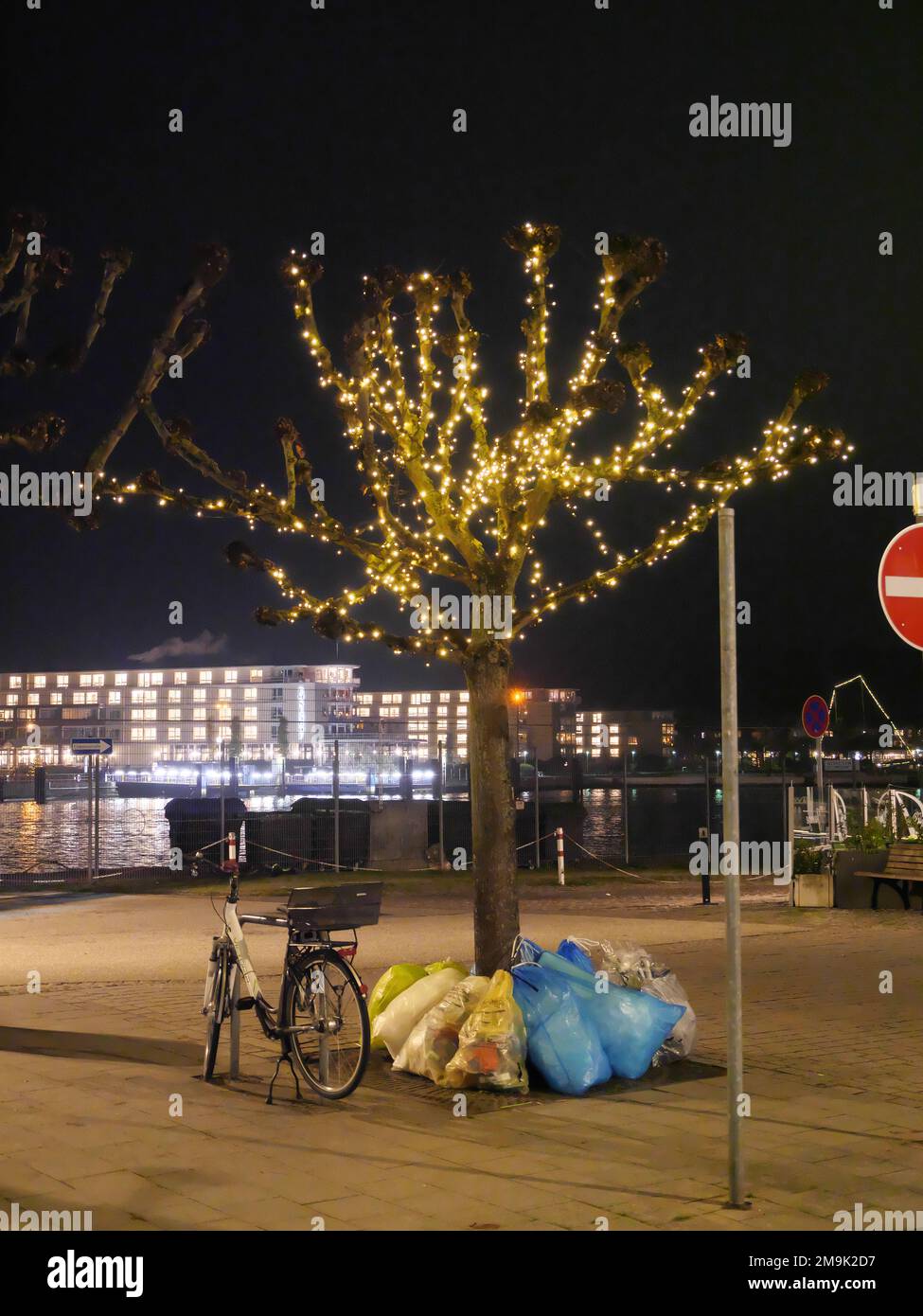 Un albero decorato con luci a LED con bicicletta e spazzatura durante il periodo natalizio a Travemünde di fronte a una nave da crociera di notte Foto Stock