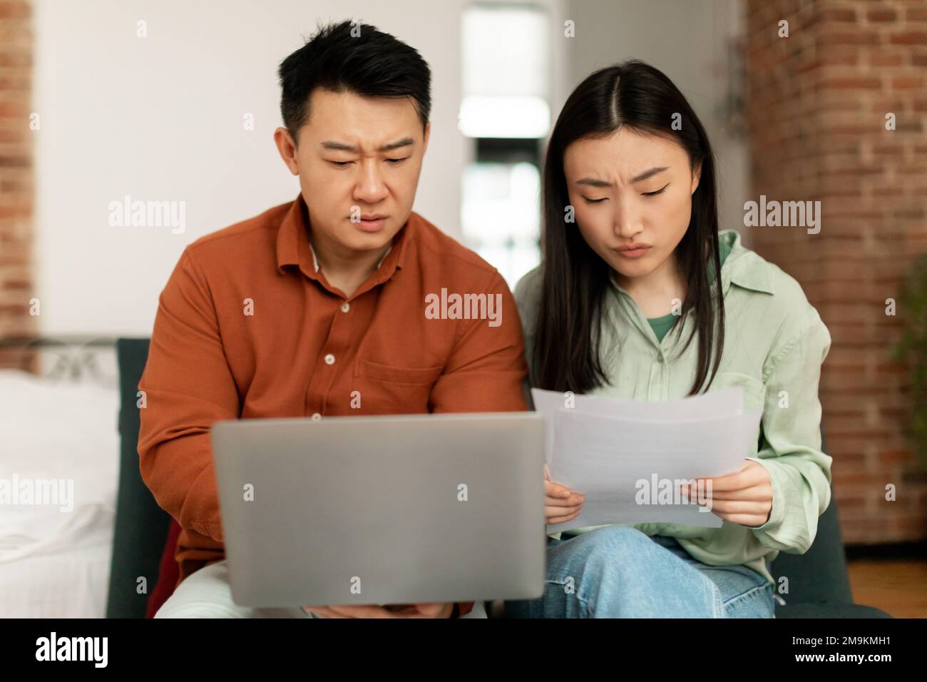 I coniugi coreani hanno sconvolto il controllo delle bollette, la lettura dei documenti seduti sul divano e utilizzando il computer portatile. Concetto di budget familiare Foto Stock