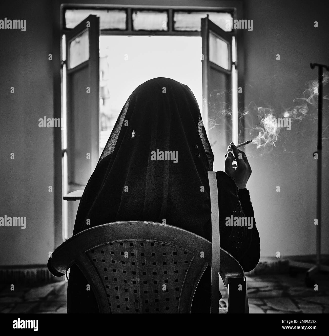 Una donna fumatrice in un hijab nero all'interno del campo di al-Hol in bianco e nero. Foto Stock