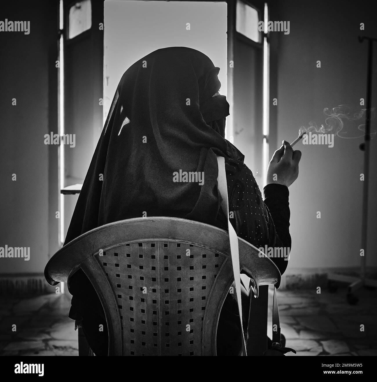 Una donna fumatrice in un hijab nero all'interno del campo di al-Hol in bianco e nero. Foto Stock