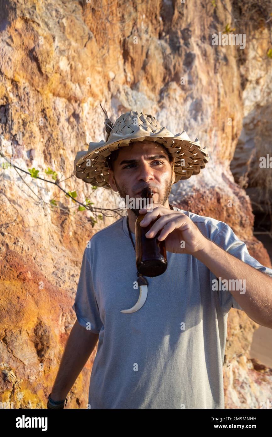 Giovane uomo con cappello di paglia che si gode una birra sulla spiaggia  durante il tramonto Foto stock - Alamy