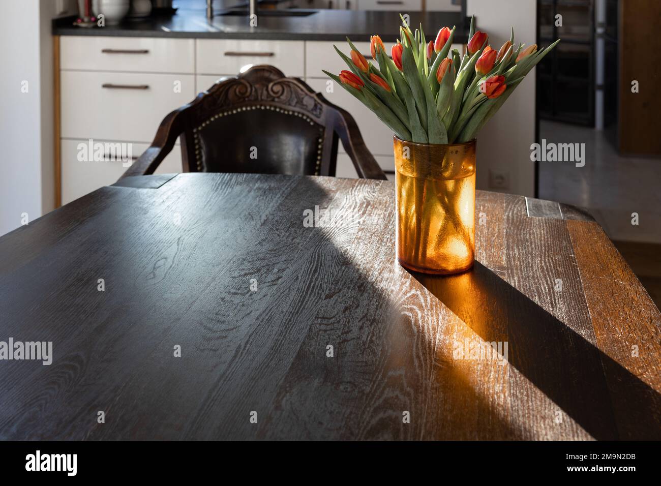 Su un massiccio tavolo di legno scuro ai raggi del sole del mattino si trova un vaso giallo con tulipani rossi. Foto Stock