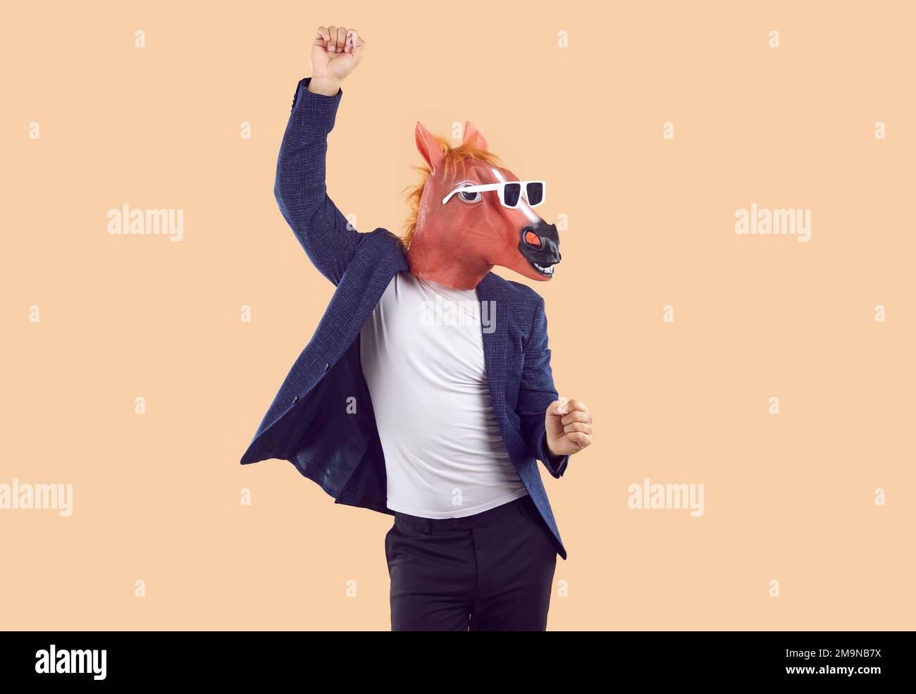 Uomo in tuta, divertente maschera a cavallo e occhiali da sole che ballano isolati su sfondo beige Foto Stock