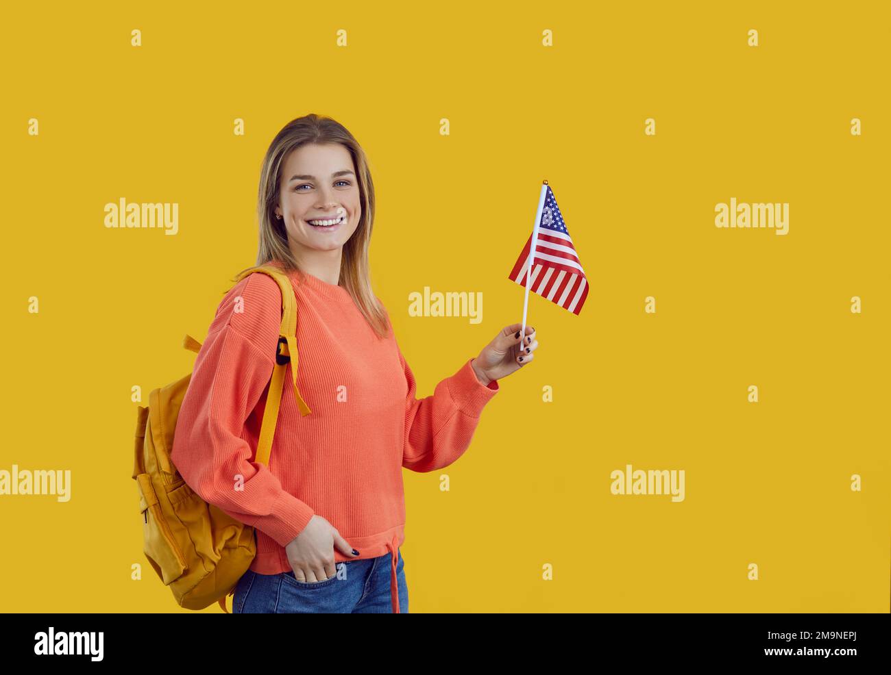Felice studente universitario in piedi su sfondo giallo, tenendo la bandiera americana e sorridendo Foto Stock
