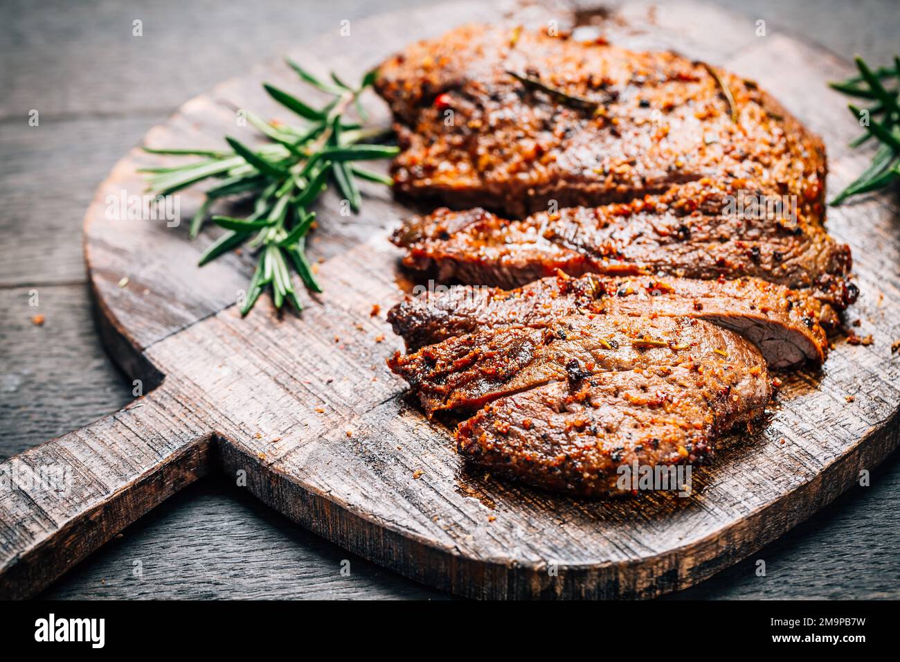 Bistecca di manzo alla griglia con spezie sul tagliere su sfondo di legno Foto Stock
