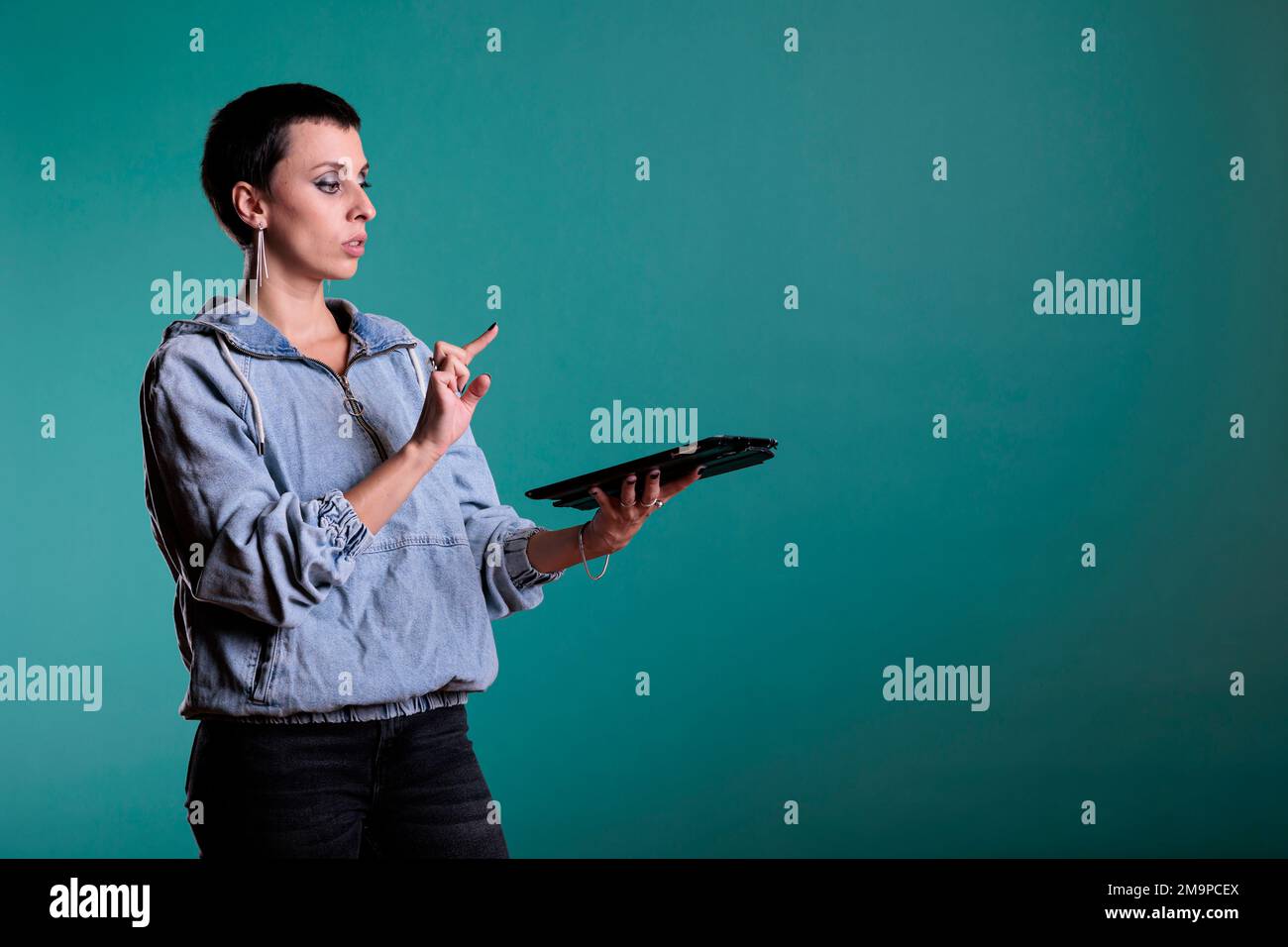 Donna sicura che tiene in mano un dispositivo digitale utilizzando l'interfaccia del database olografico con realtà aumentata, in piedi in studio su uno sfondo isolato. Adulto che ha esperienza futuristica utilizzando la tecnologia. Foto Stock