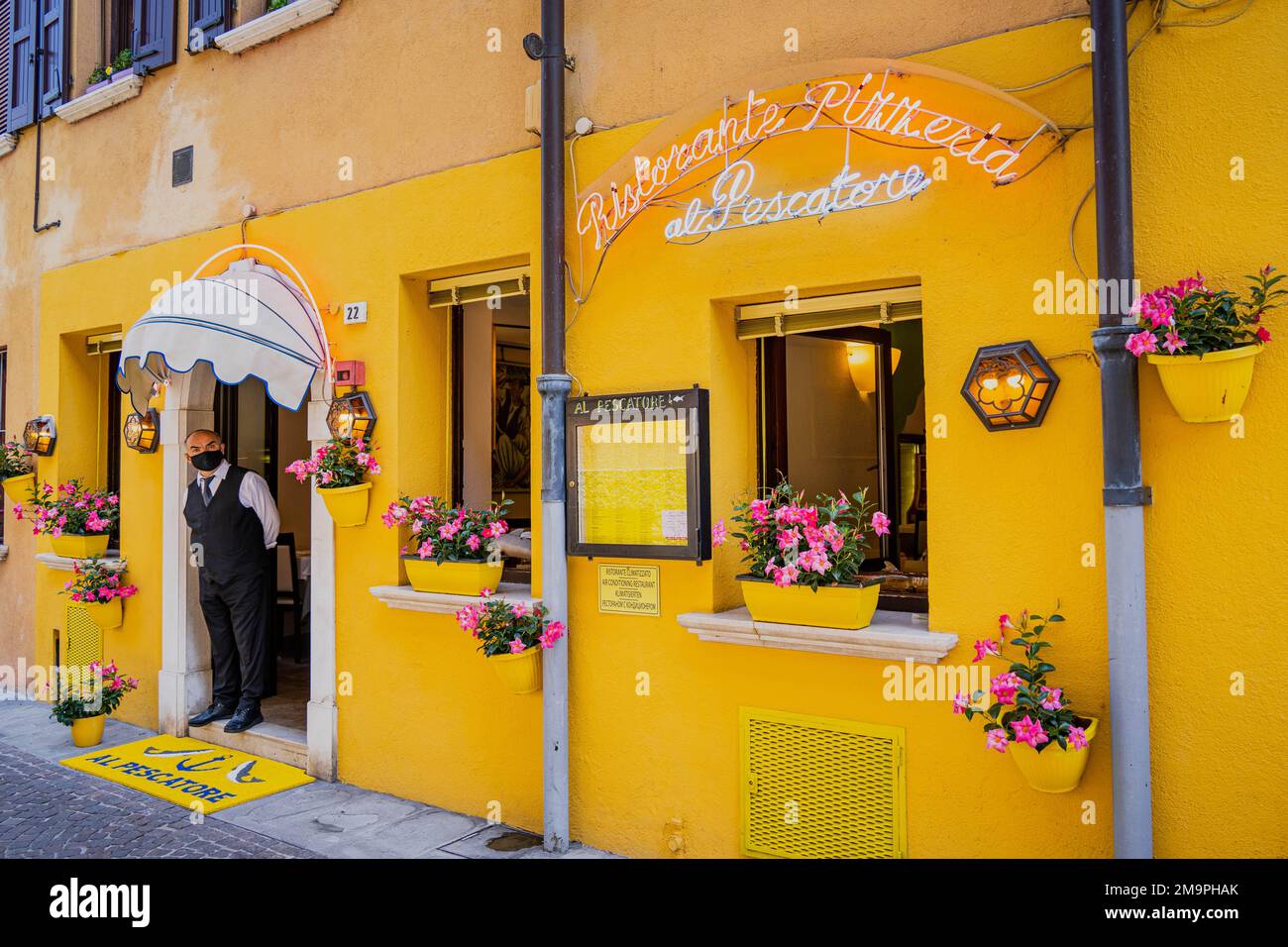 Un cameriere si trova alla porta di un ristorante di colore giallo a Sirmione Foto Stock