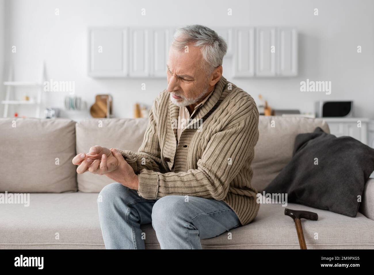 uomo anziano con sindrome di parkinson che soffre di tremore nelle mani  mentre si siede sul divano vicino alla canna da camminata, immagine di  scorta Foto stock - Alamy