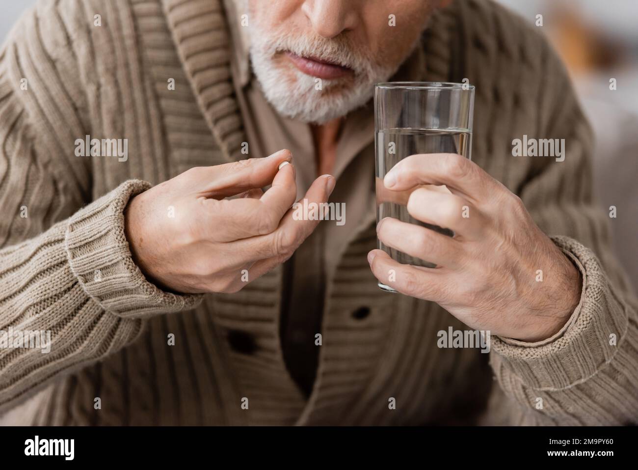 vista parziale dell'uomo anziano con la pillola del morbo di parkinson e il vetro di acqua nelle mani tremanti, immagine di scorta Foto Stock