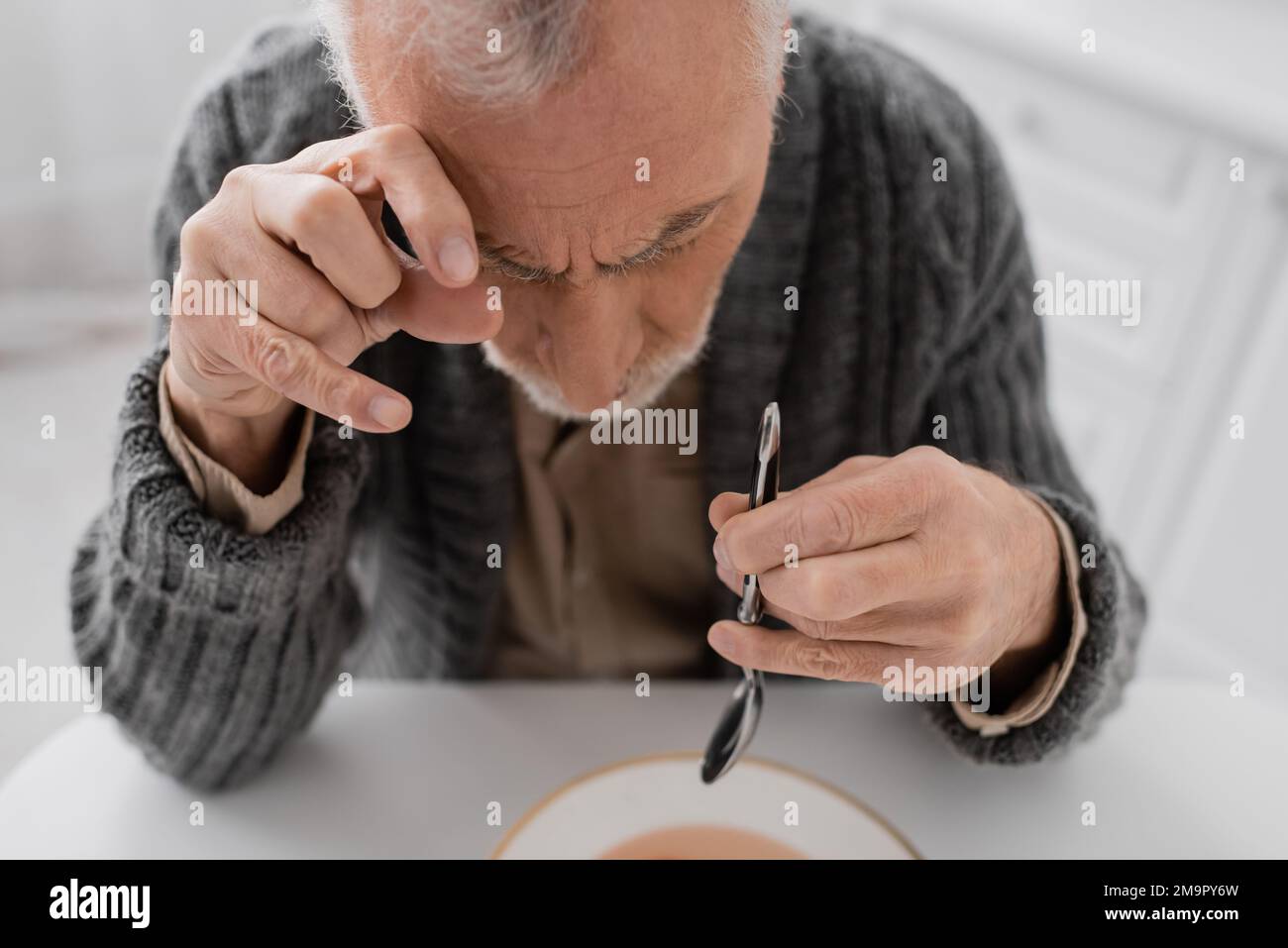 uomo anziano affetto da morbo di parkinson e tremore mani seduto con  cucchiaio durante il pranzo in cucina, immagine stock Foto stock - Alamy