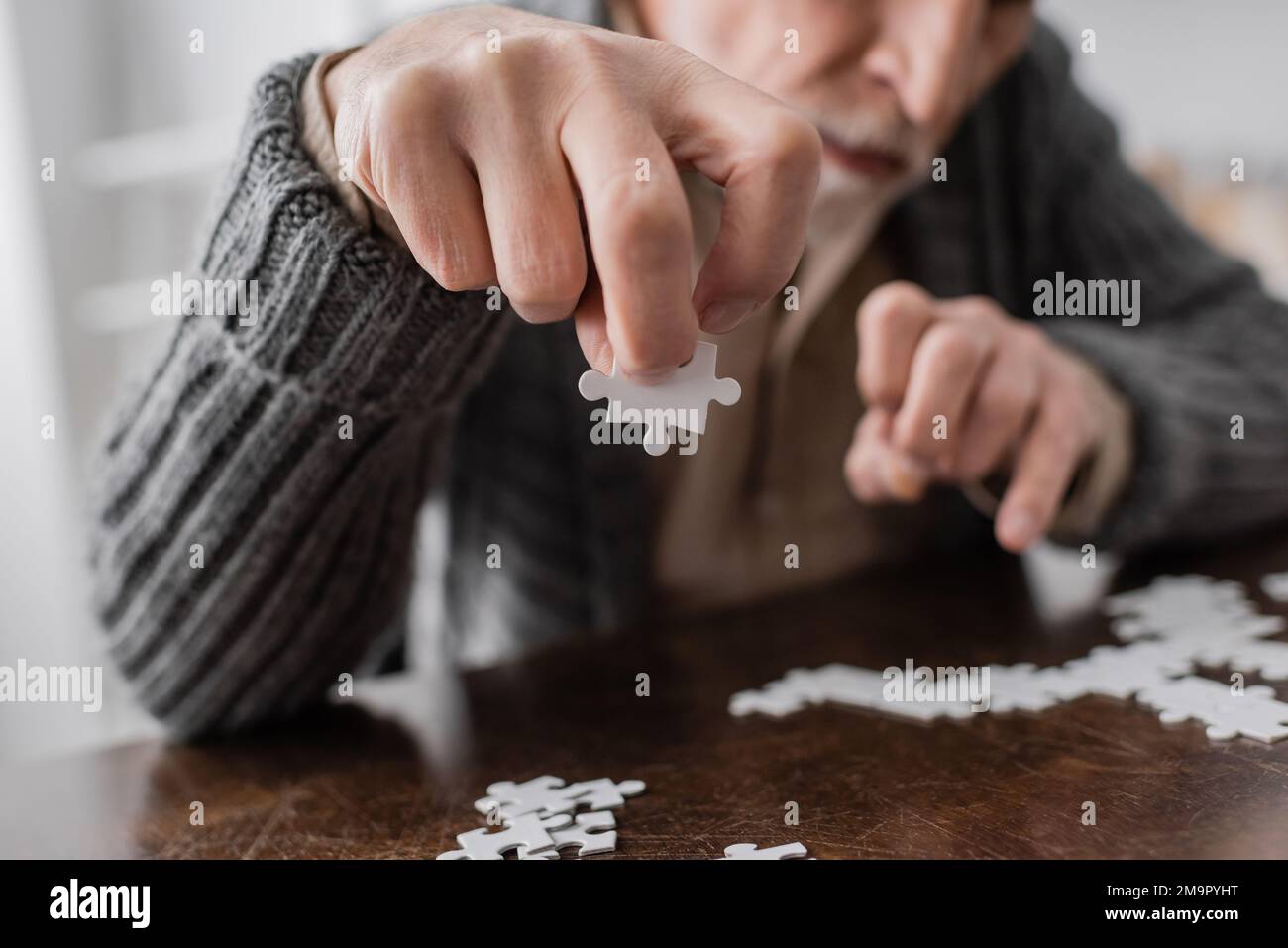 vista parziale dell'uomo sfocato con sindrome di parkinson che tiene l'elemento di puzzle jigsaw in mano tremolante, immagine di scorta Foto Stock