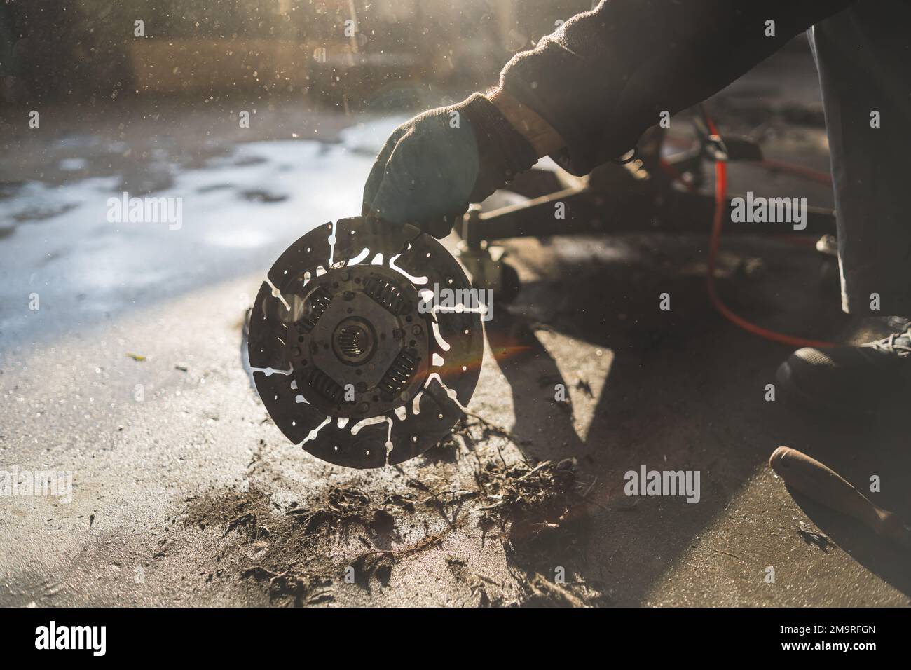 Mani di meccanico che tiene una vecchia frizione grigia argento rotta ad un negozio di riparazione auto. Foto di alta qualità Foto Stock